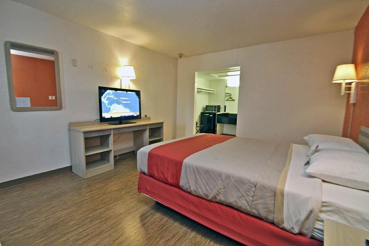 A hotel room with a bed, a desk with a computer, a TV, and a mirror.
