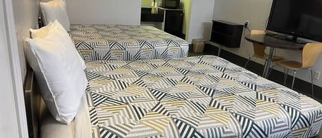 Quarto duplo com duas camas, uma escrivaninha, uma televisão e um espelho.