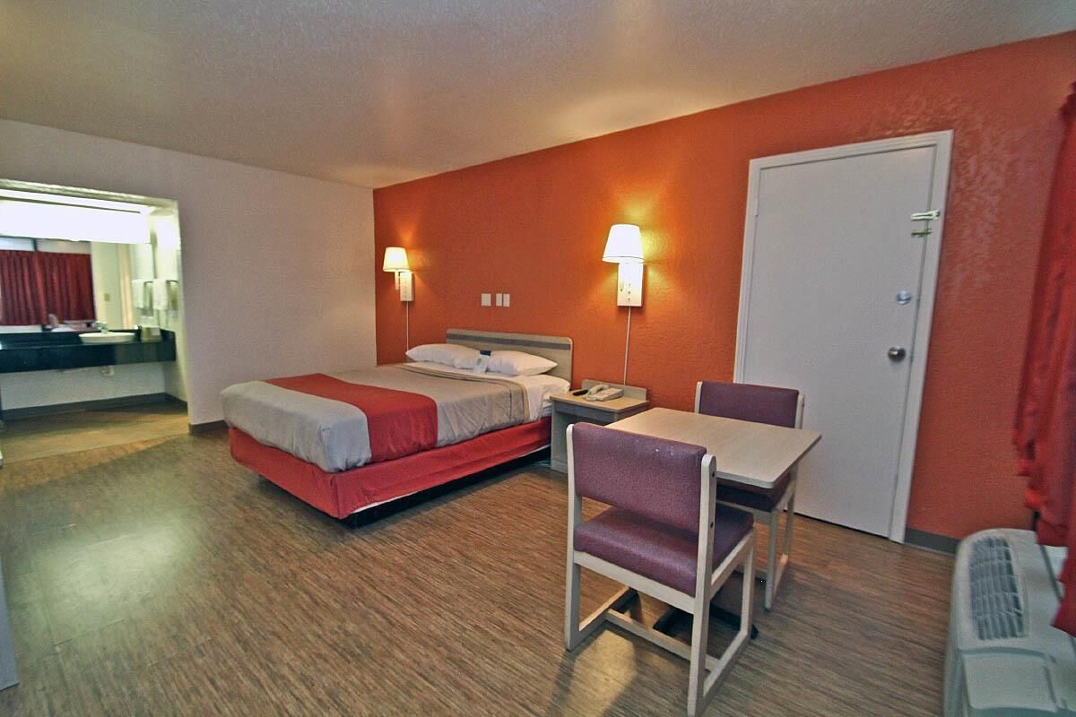 A hotel room with a bed, bedside table, chair, and a desk with a chair.