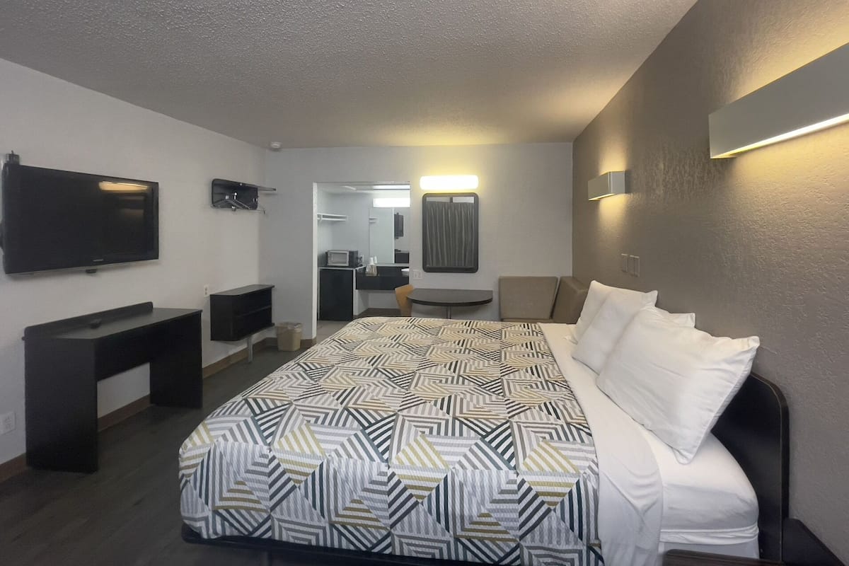 A hotel room with a large bed, a TV, a desk, and a mirror.