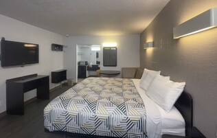 A hotel room with a large bed, a TV, a desk, and a mirror.