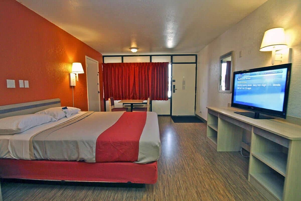 A hotel room with a bed, a desk with a computer, a TV, and a red curtain.