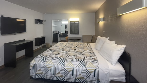A hotel room with a large bed, a desk, a TV, and a bathroom visible through an open door. - Motel 6 Sallisaw, OK (Sallisaw)