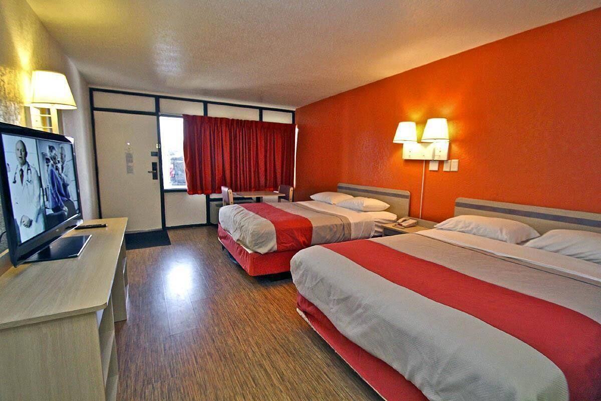 A hotel room with two beds, a TV, a desk, and a window with red curtains.