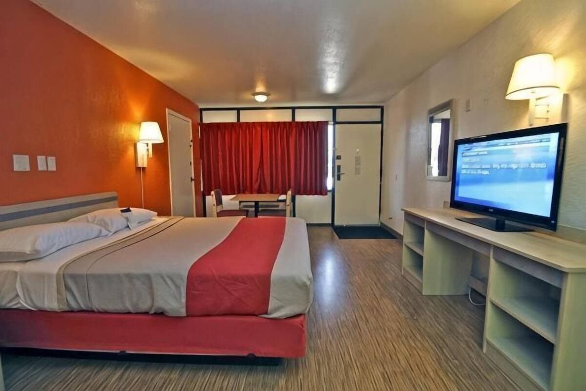 A hotel room with a bed, a desk, a television, and a red curtain.