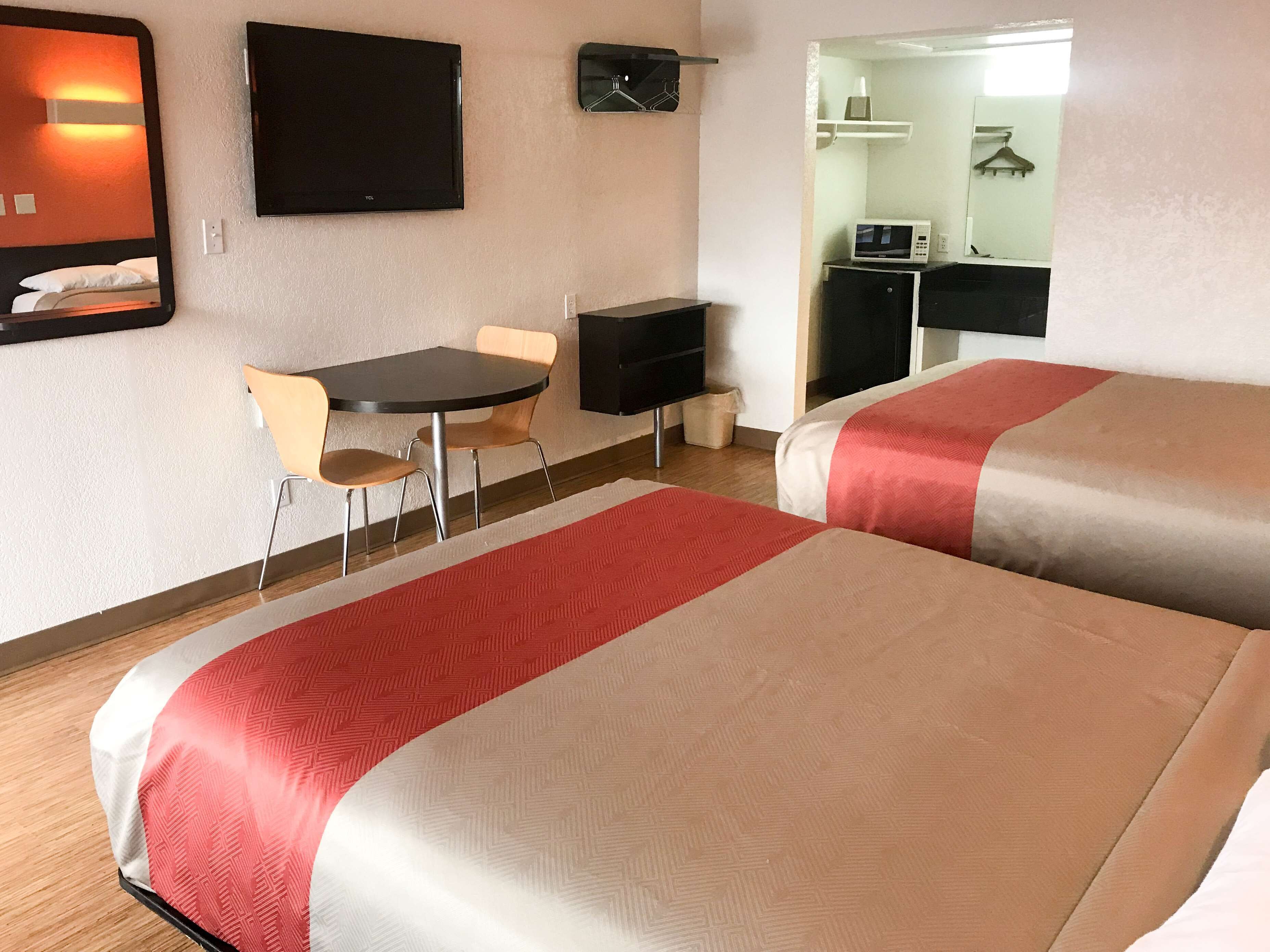 Une chambre d’hôtel avec deux lits, une petite table avec des chaises, un téléviseur et un four à micro-ondes.