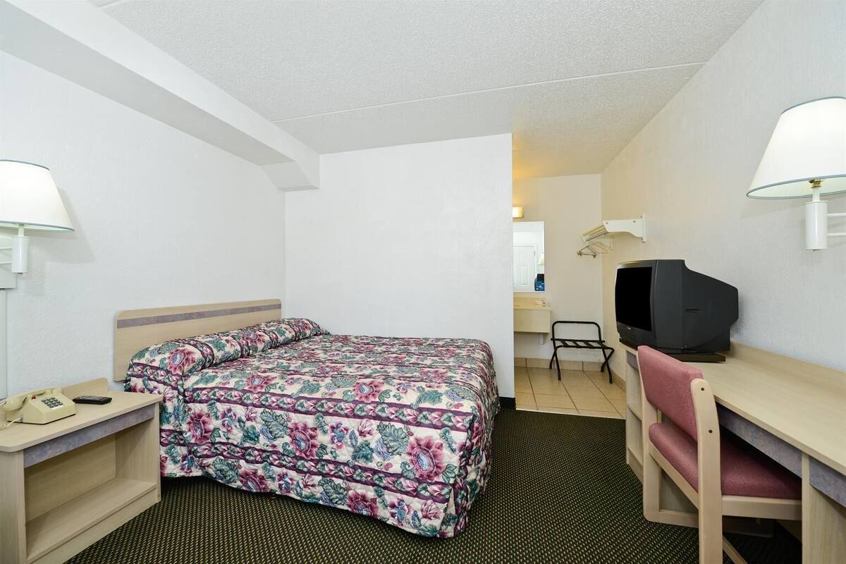 A hotel room with a bed, desk, chair, television, and lamps.