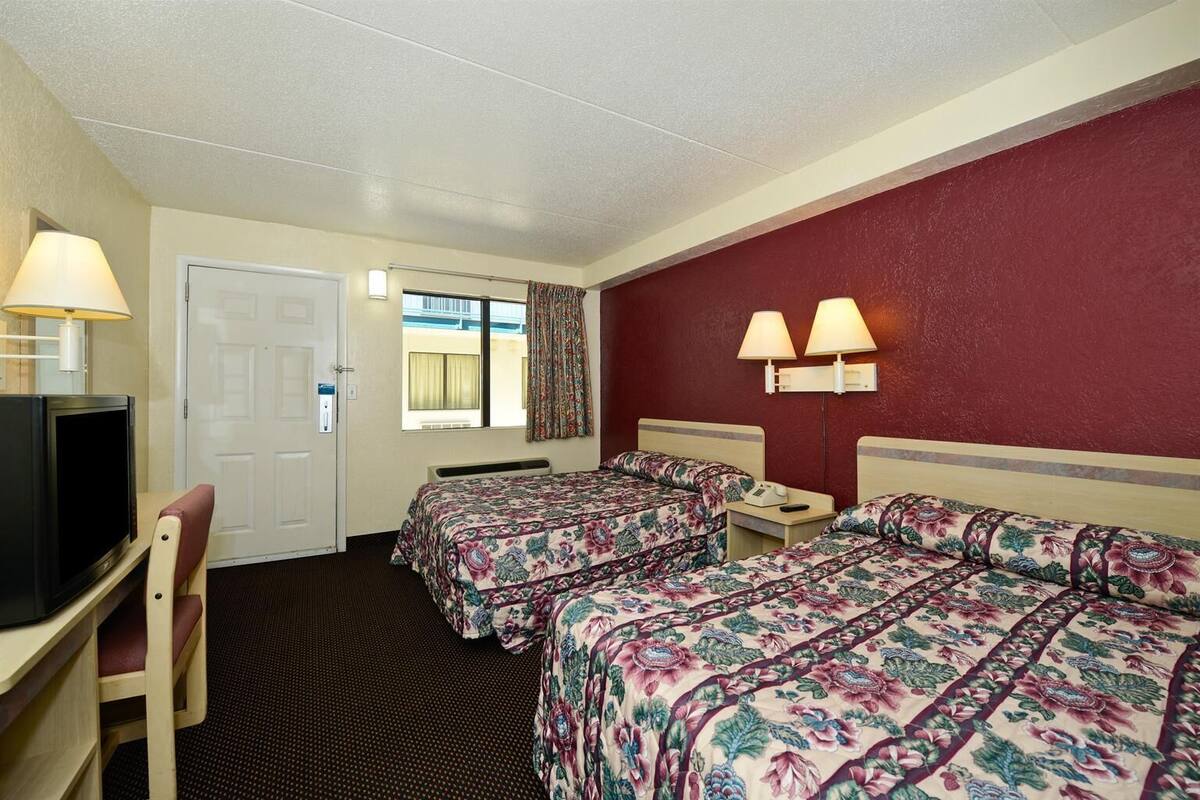 A hotel room with two beds, a desk with a television, and a window with curtains.