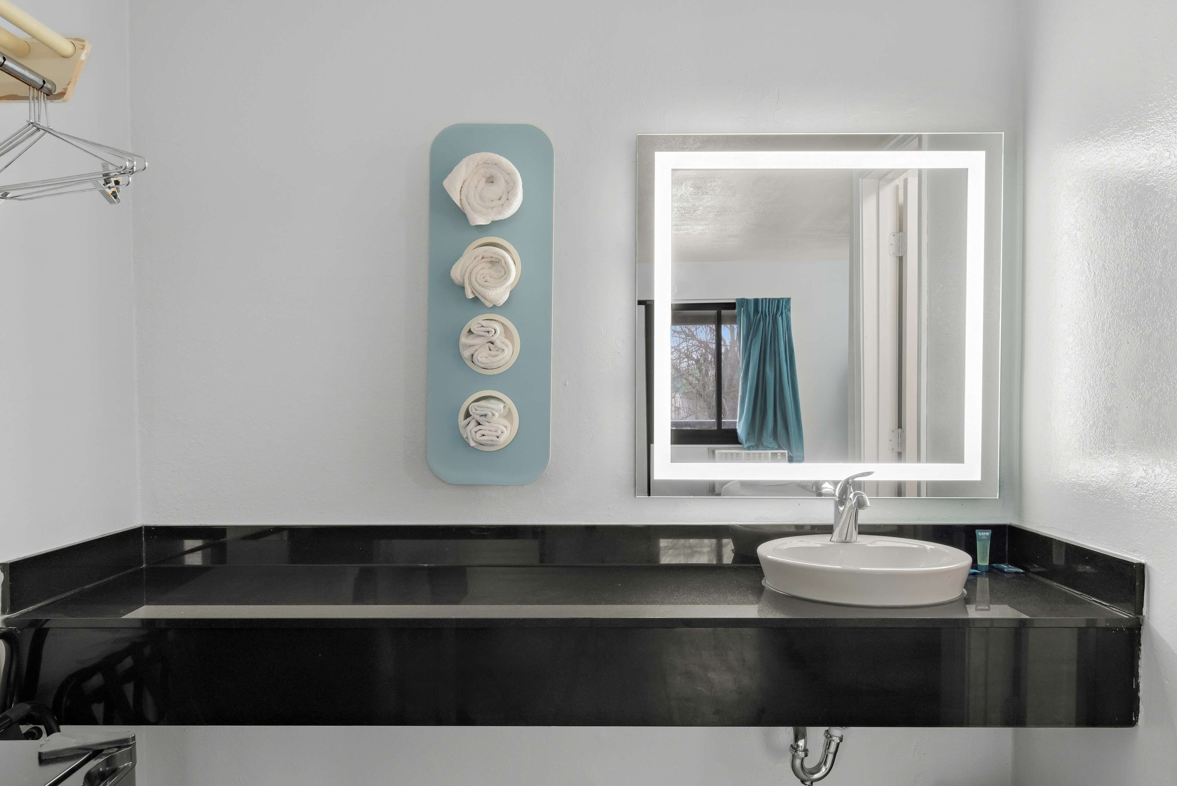 A modern bathroom with a black countertop, a white sink, and a mirror. There are four rolled towels on a blue towel rack.