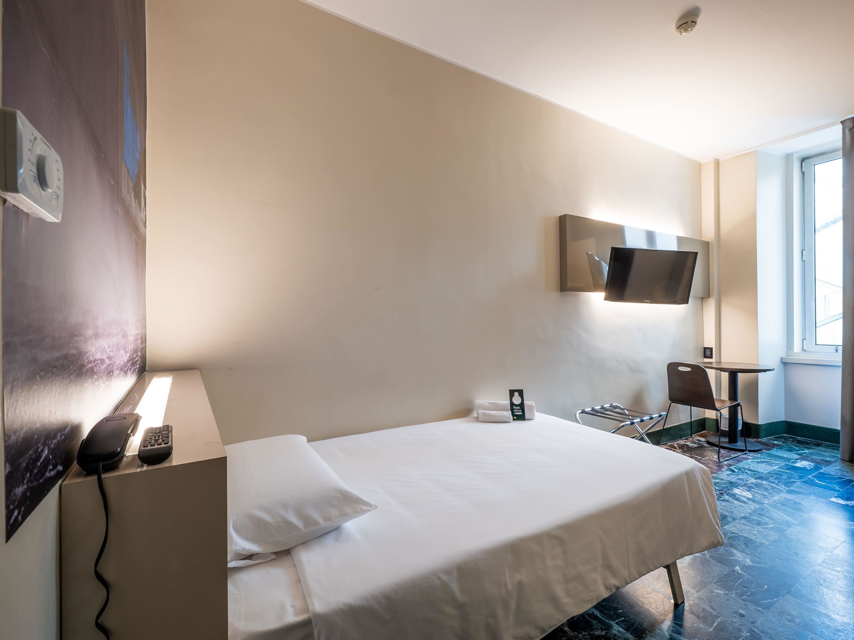 Ein Hotelzimmer mit Bett, Wandfernseher, Schreibtisch und Stuhl sowie einem Fenster.