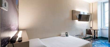 Ein Hotelzimmer mit Bett, Wandfernseher, Schreibtisch und Stuhl sowie einem Fenster.