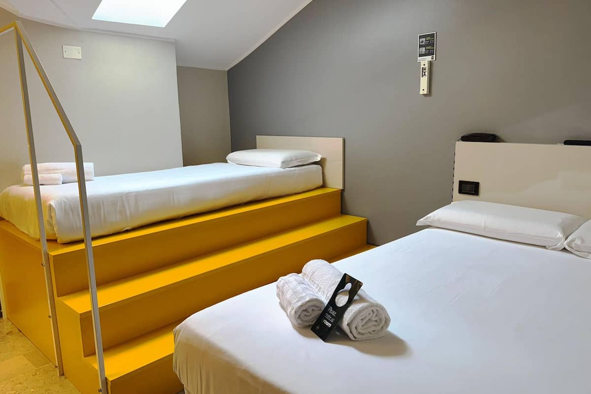 A hotel room with two beds, a staircase, a skylight, and a control panel on the wall.