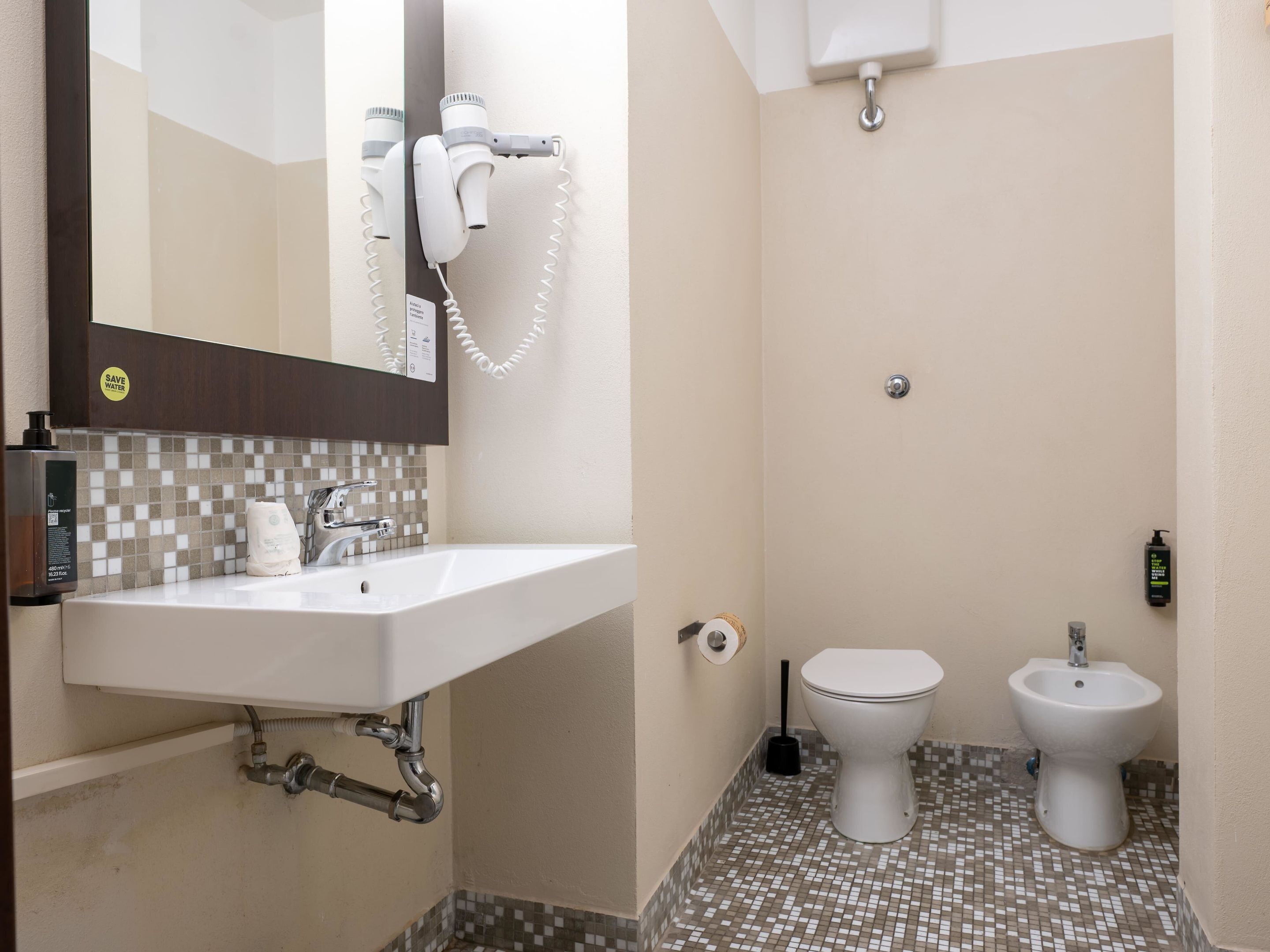 A bathroom with a sink, toilet, bidet, and a mirror.