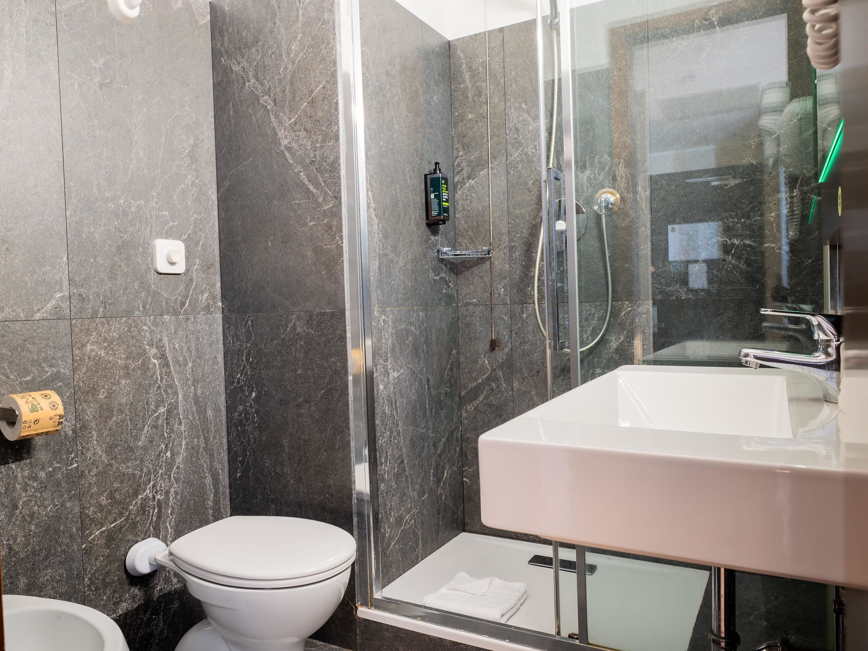 Une salle de bain moderne avec une douche à parois de verre, des toilettes blanches et un lavabo avec un miroir.