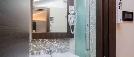 Ein Badezimmer mit einem weißen Waschbecken, einem Spiegel, einem Fön und einer Dusche.