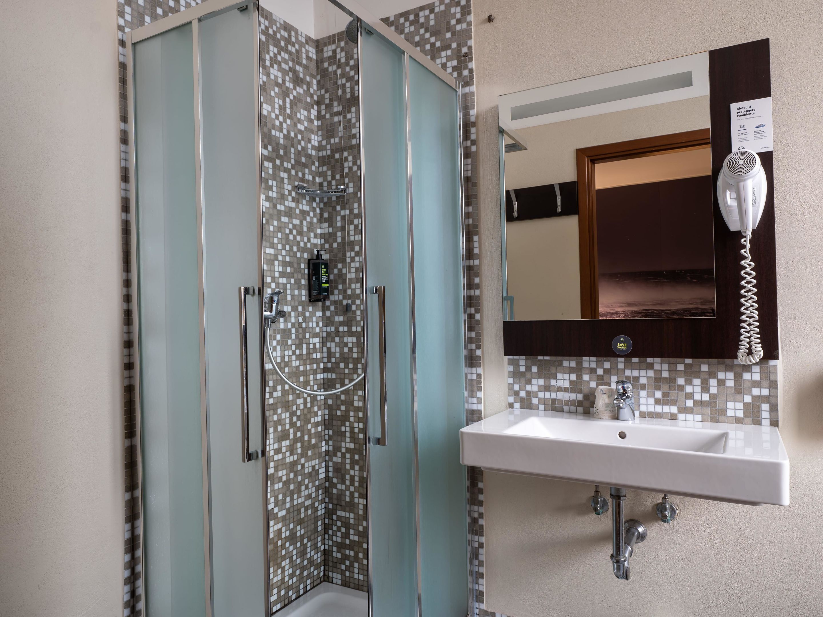 A modern bathroom with a glass-enclosed shower, a white sink, and a mirror with a mounted telephone.