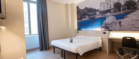 Habitación de hotel con cama, escritorio, silla, ventana con cortinas y un gran mural en la pared que representa un edificio junto al agua.