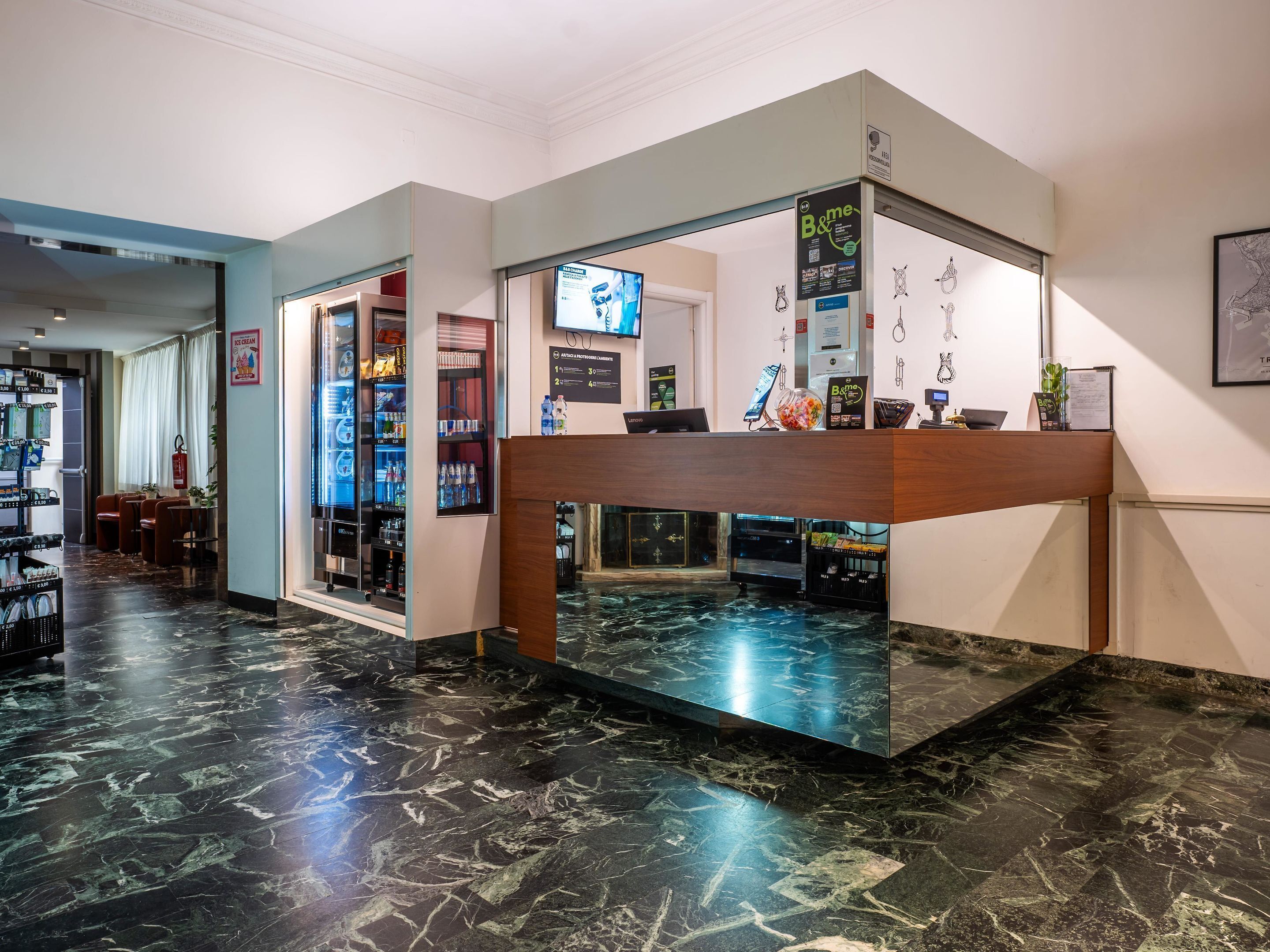 A reception area with a marble floor, a counter with a digital screen, and a wall-mounted TV.