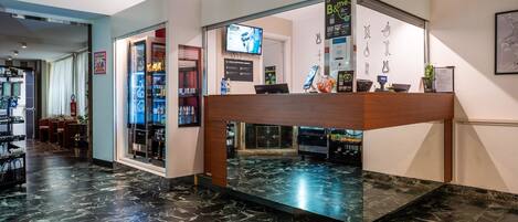 A reception area with a marble floor, a counter with a digital screen, and a wall-mounted TV.