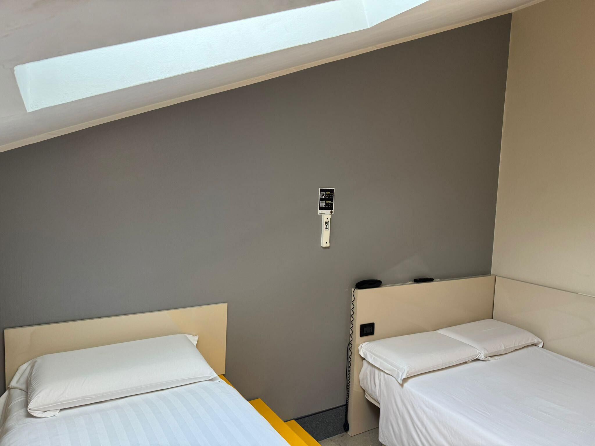 Ein kleines, modernes Hotelzimmer mit zwei Einzelbetten, einem Schreibtisch und einem kleinen Fenster.