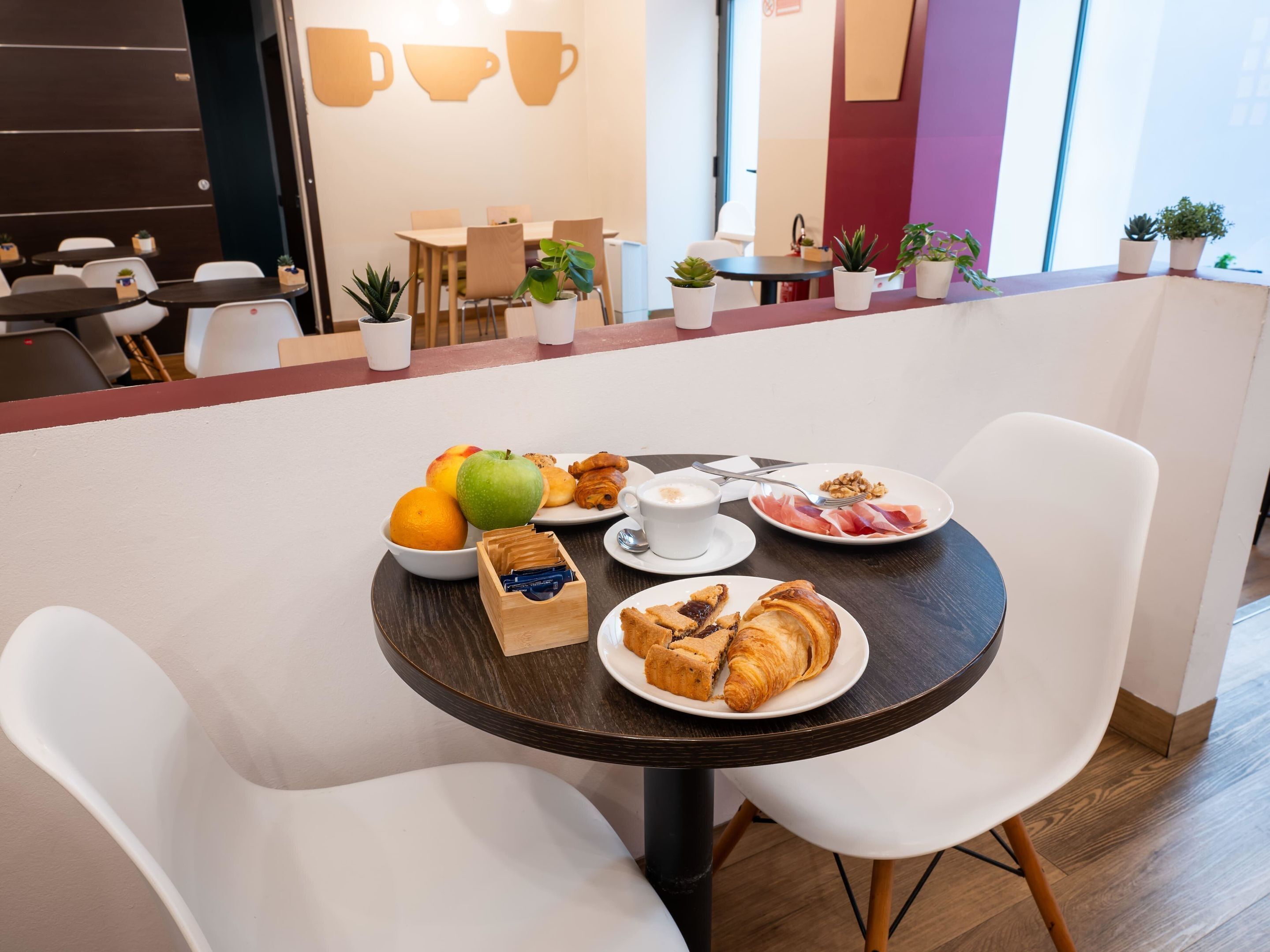 A dining area with a table set for breakfast, including fruits, pastries, and a cup of coffee.