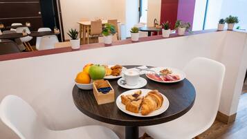 A dining area with a table set for breakfast, including fruits, pastries, and a cup of coffee.