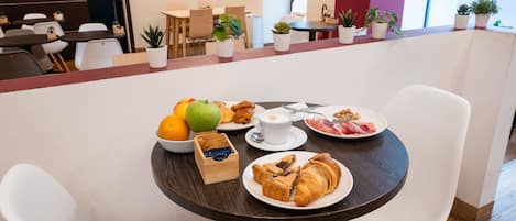 A dining area with a table set for breakfast, including fruits, pastries, and a cup of coffee.