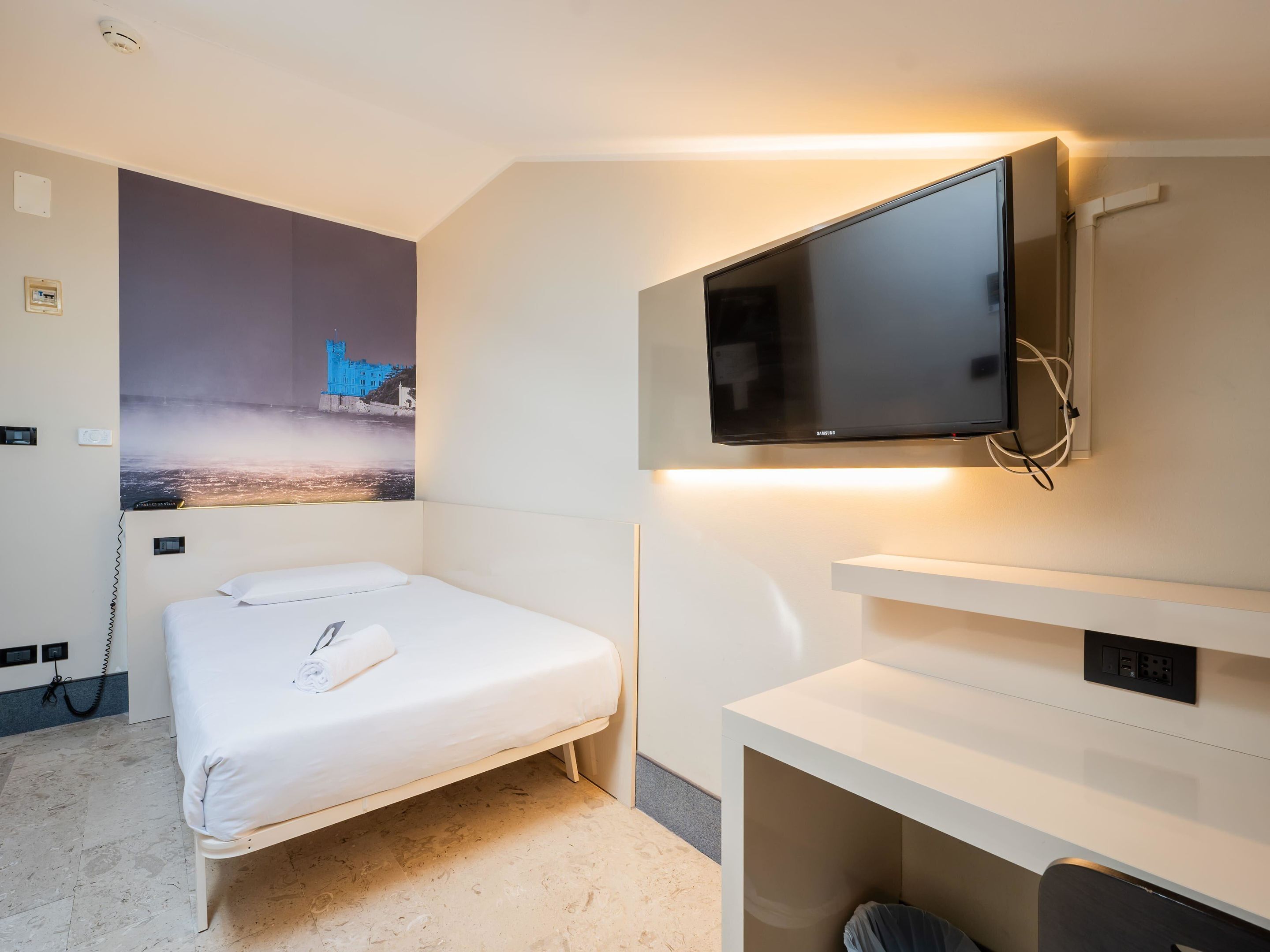 Habitación de hotel con cama, televisor de pantalla plana en la pared, escritorio con silla y un cartel de un castillo en la pared.