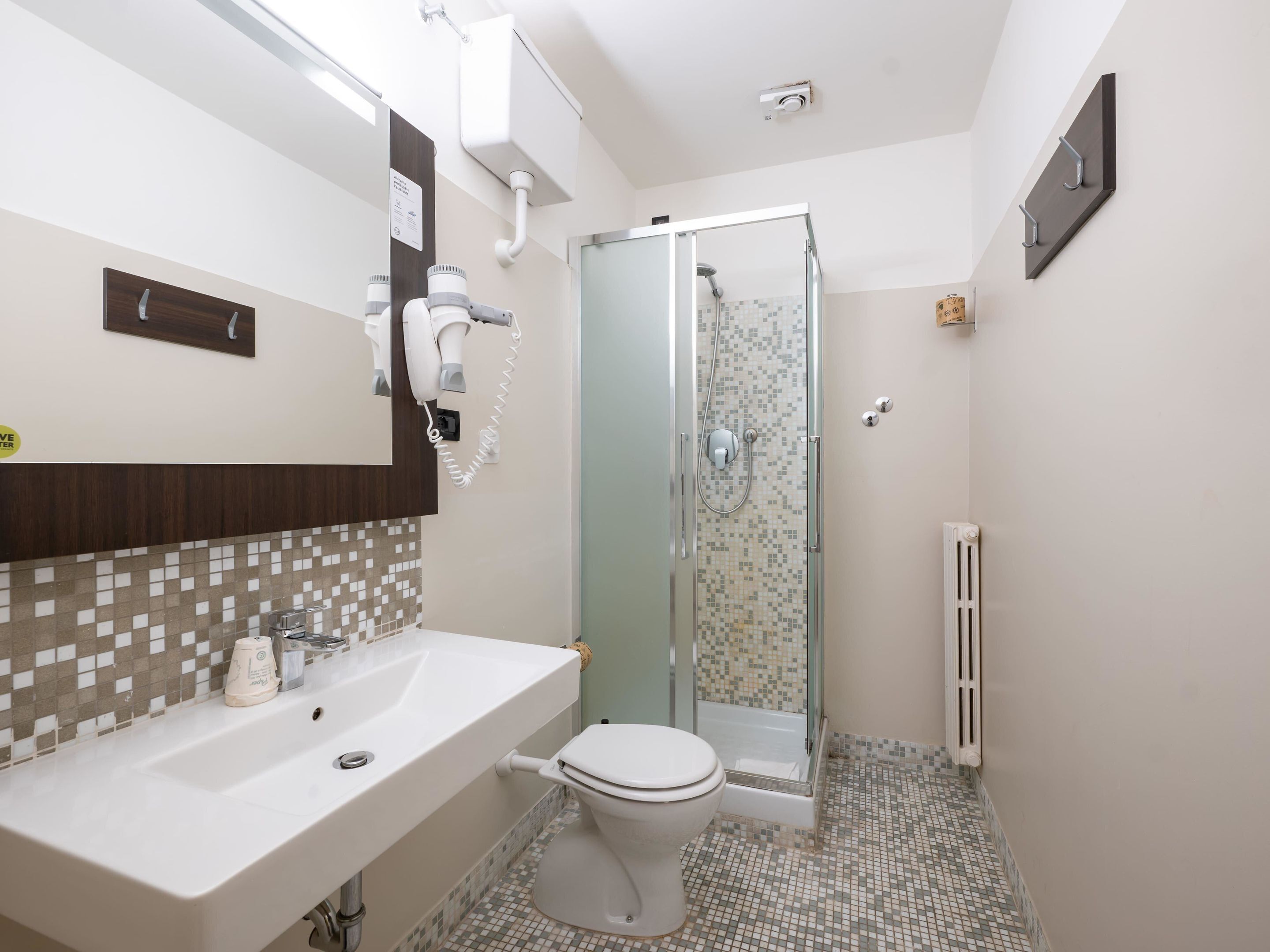 Une salle de bain avec un lavabo blanc, des toilettes, une cabine de douche en verre et un miroir surmonté d’un panneau en bois.