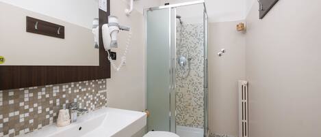 A bathroom with a white sink, a toilet, a glass shower enclosure, and a mirror with a wooden panel above it.