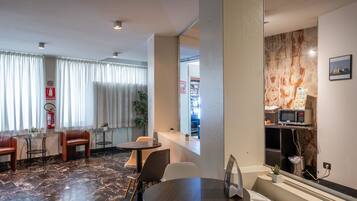 Hall d'albergo con pavimento in marmo, sedute in pelle, un piccolo tavolo con sedie, un forno a microonde, una macchina distributrice e un estintore.