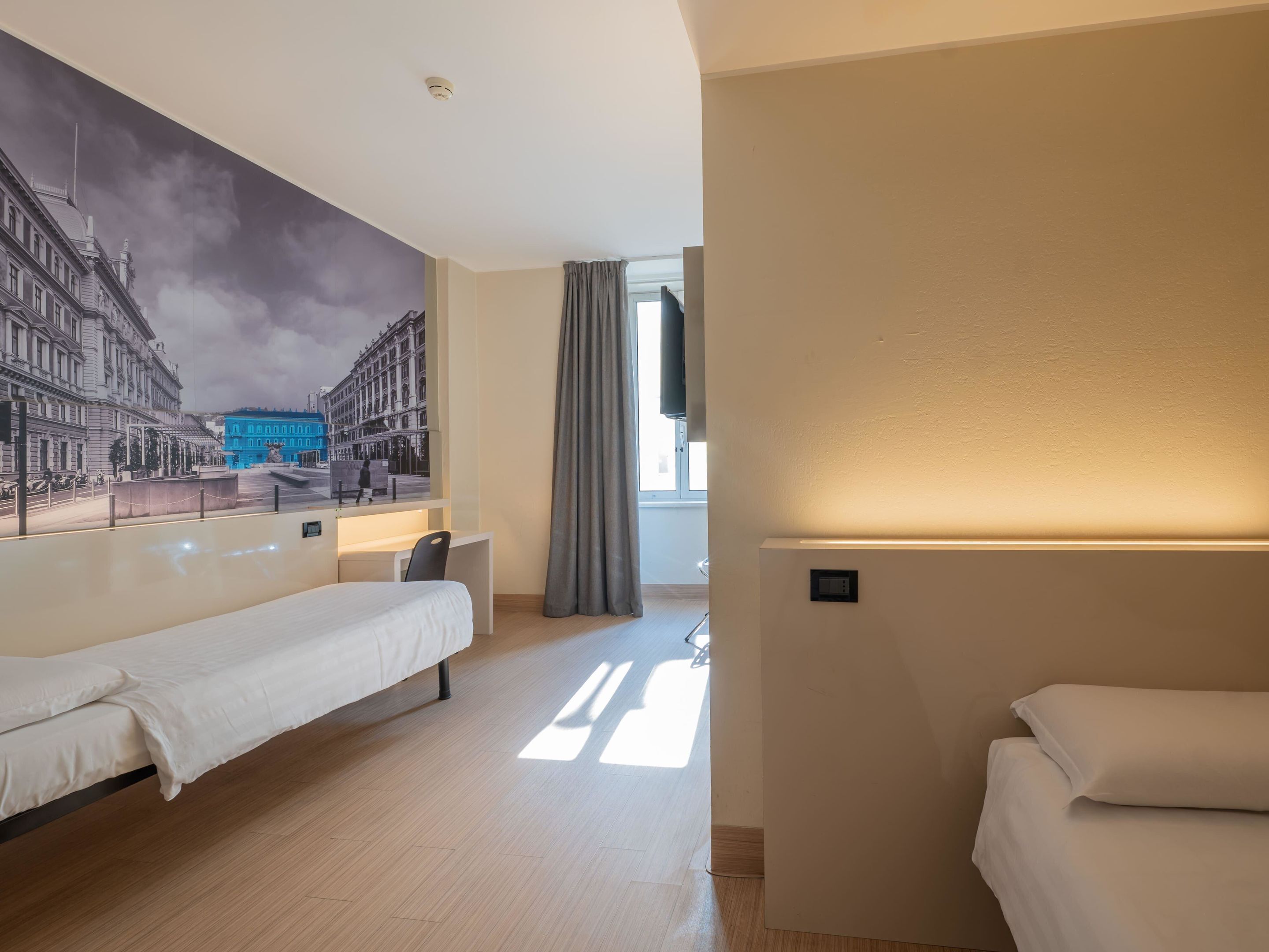 Habitación de hotel con cama, escritorio y un gran mural de un paisaje urbano en la pared.