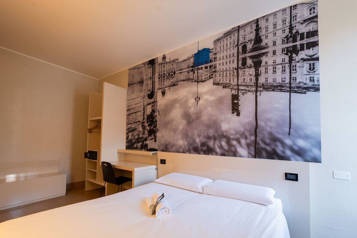 A hotel room with a large bed, a desk, and a chair.