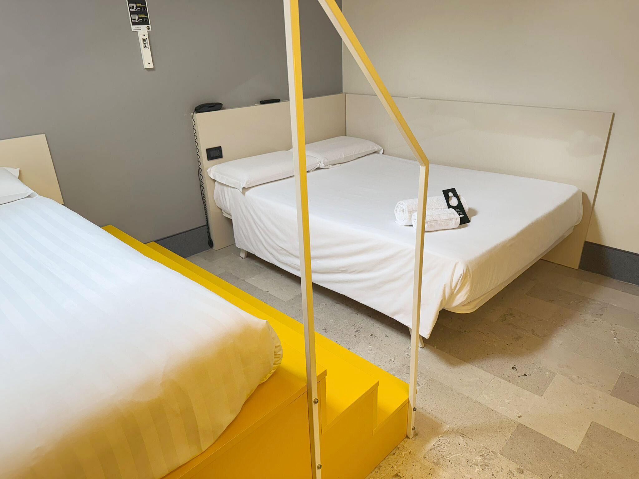 A room with two single beds, a yellow partition, and a wall-mounted phone.