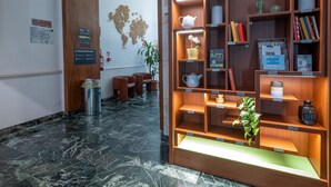 A reception area with a wooden bookshelf, seating, a world map on the wall, and a marble floor. - B&B Hotel Trieste (Trieste)