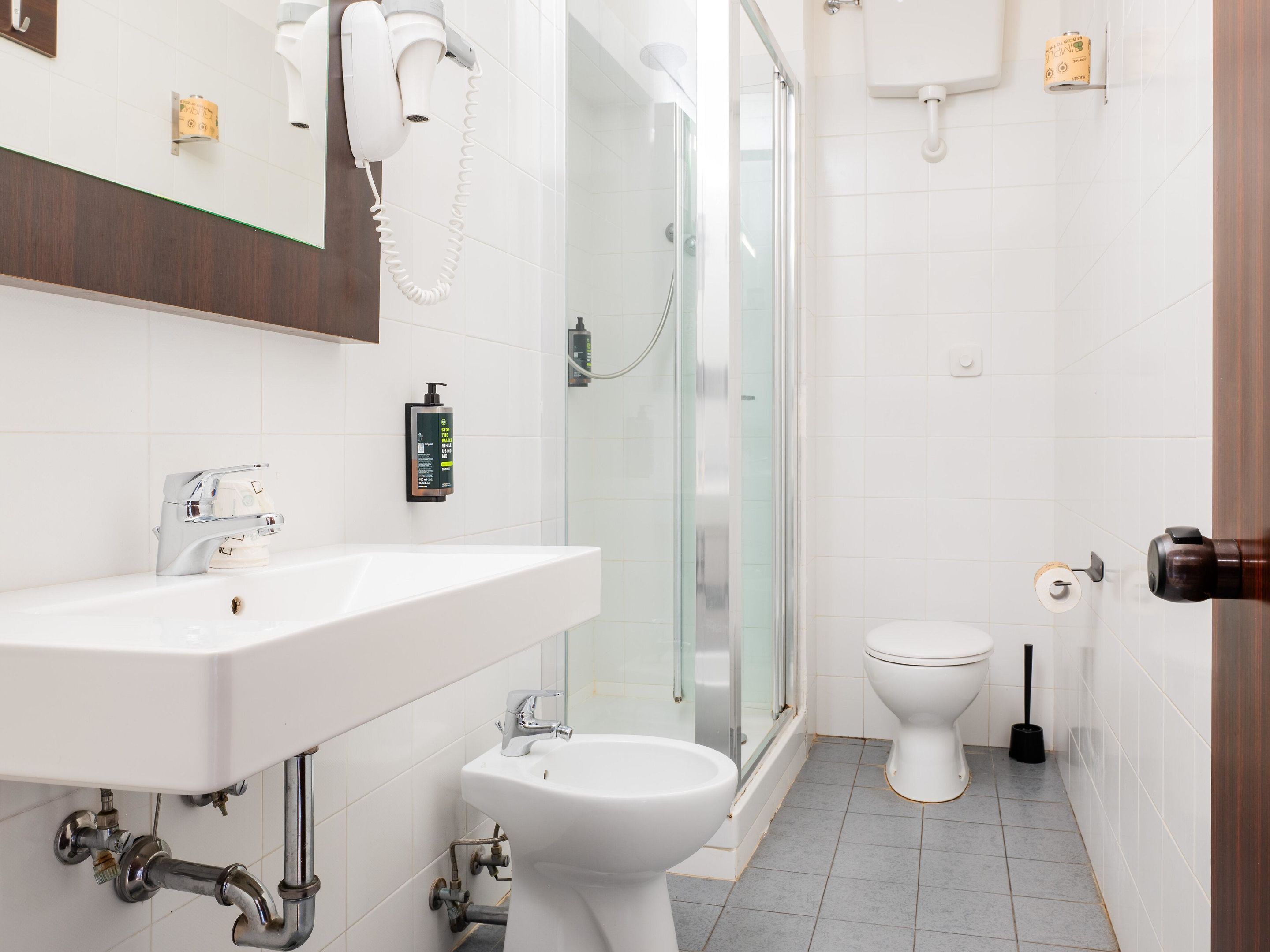 A modern bathroom with a white sink, bidet, and glass shower enclosure.