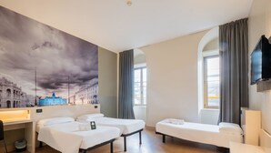 A hotel room with two beds, a desk, a TV, and a large window with curtains. - B&B Hotel Trieste (Trieste)