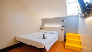 Camera d'albergo con un letto, una TV a parete, una piccola scrivania e un contenitore giallo.