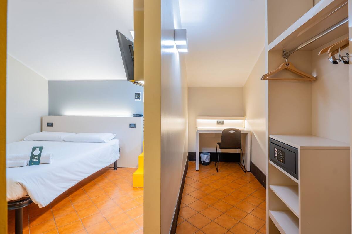 A compact hotel room with a bed, a desk, and a wardrobe.