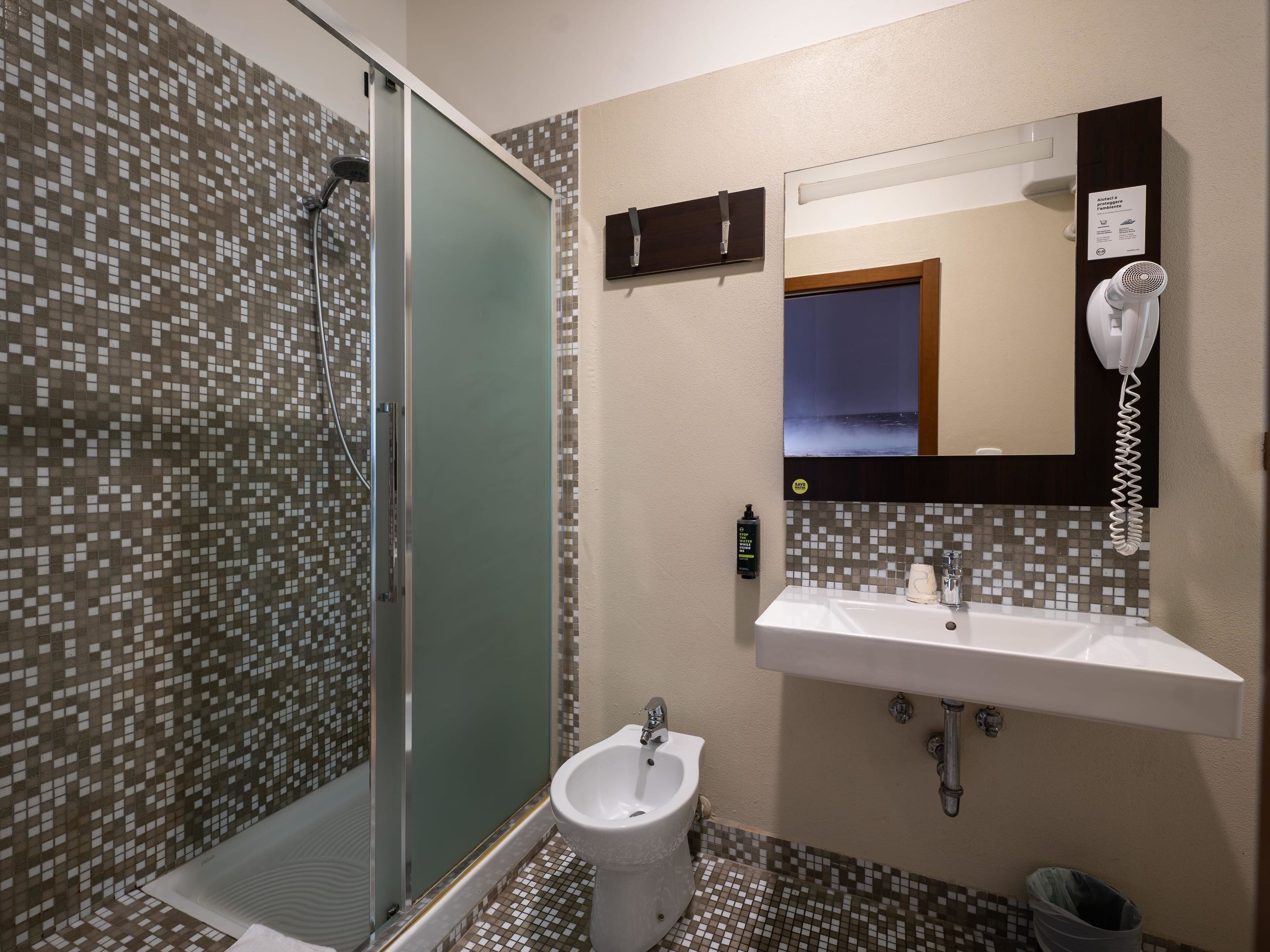 Baño con cabina de ducha de vidrio, un bidé, un lavamanos con espejo y un secador de pelo montado en la pared.