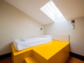 Un letto singolo in una stanza con soffitto spiovente e finestra a lucernario.