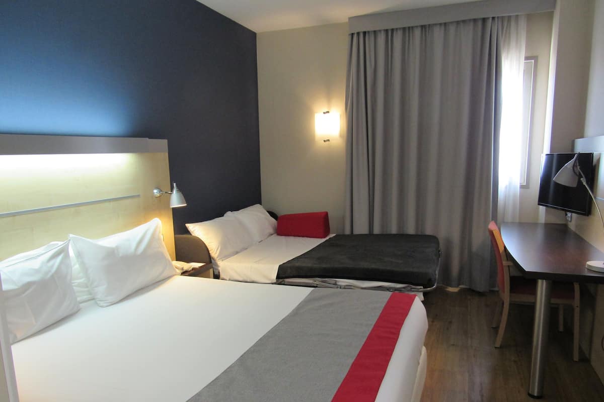 A hotel room with two beds, a desk, a chair, a TV, and a window with curtains.