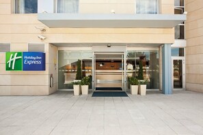 A Holiday Inn Express hotel entrance with a glass door, potted plants, and a security camera.