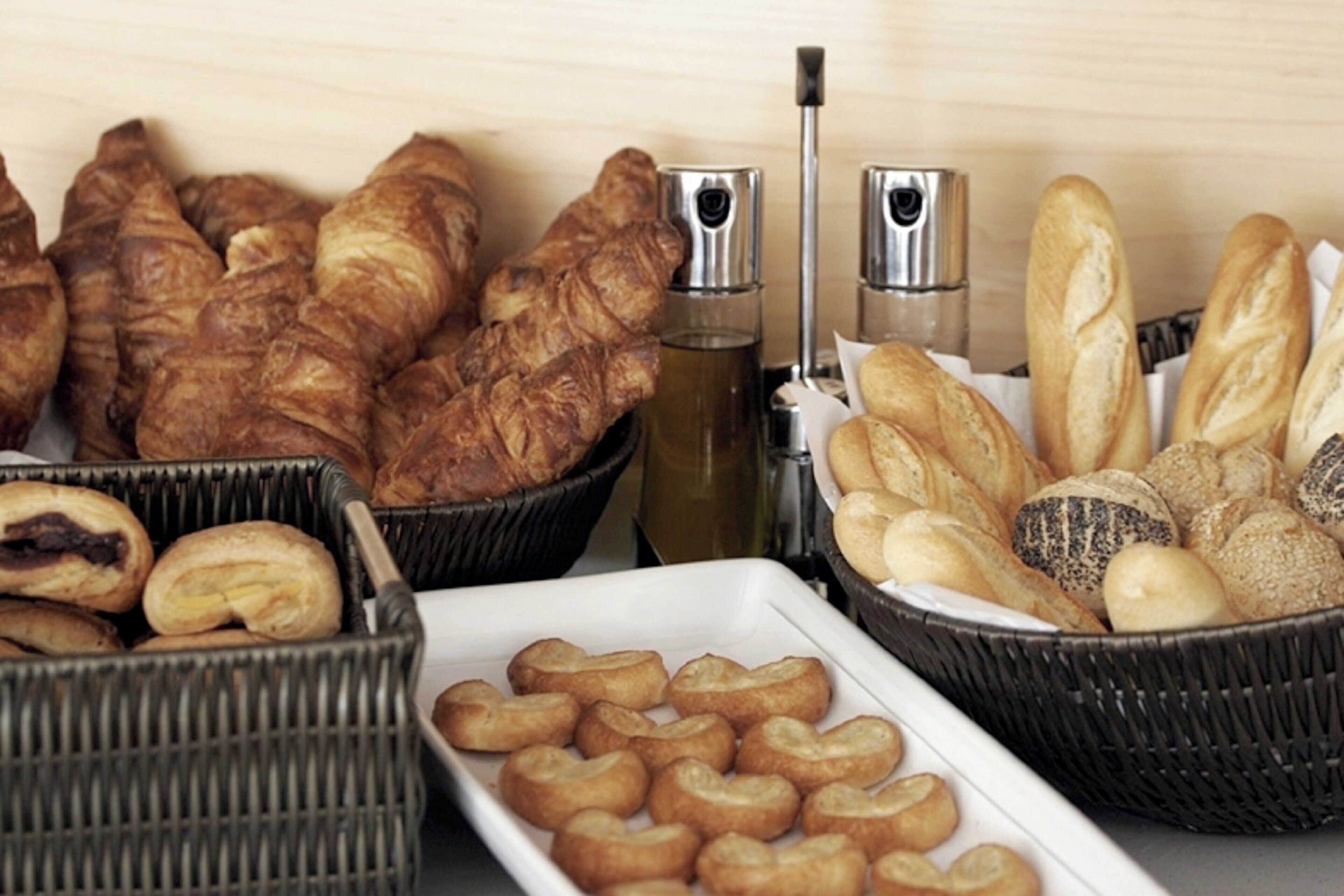 Varietat de pa i pastissos, incloent croissants, pa de motlle i pastisseria, presentats en cistades i un plat.