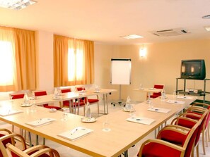 Uma sala de conferência com uma mesa comprida, cadeiras, um quadro branco e uma televisão.