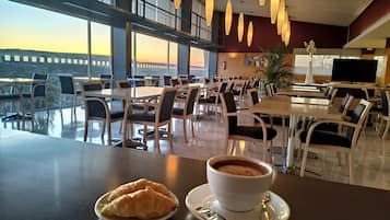 Un comedor con mesas y sillas, una taza de café y un croissant en un plato.