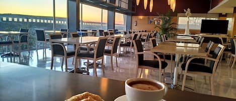 A dining area with tables and chairs, a cup of coffee, and a croissant on a plate.