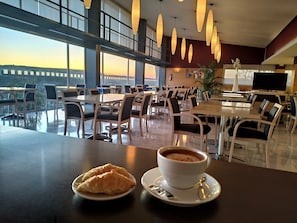 A dining area with tables and chairs, a cup of coffee, and a croissant on a plate. - Holiday Inn Express Madrid - Rivas by IHG (Rivas-Vaciamadrid)