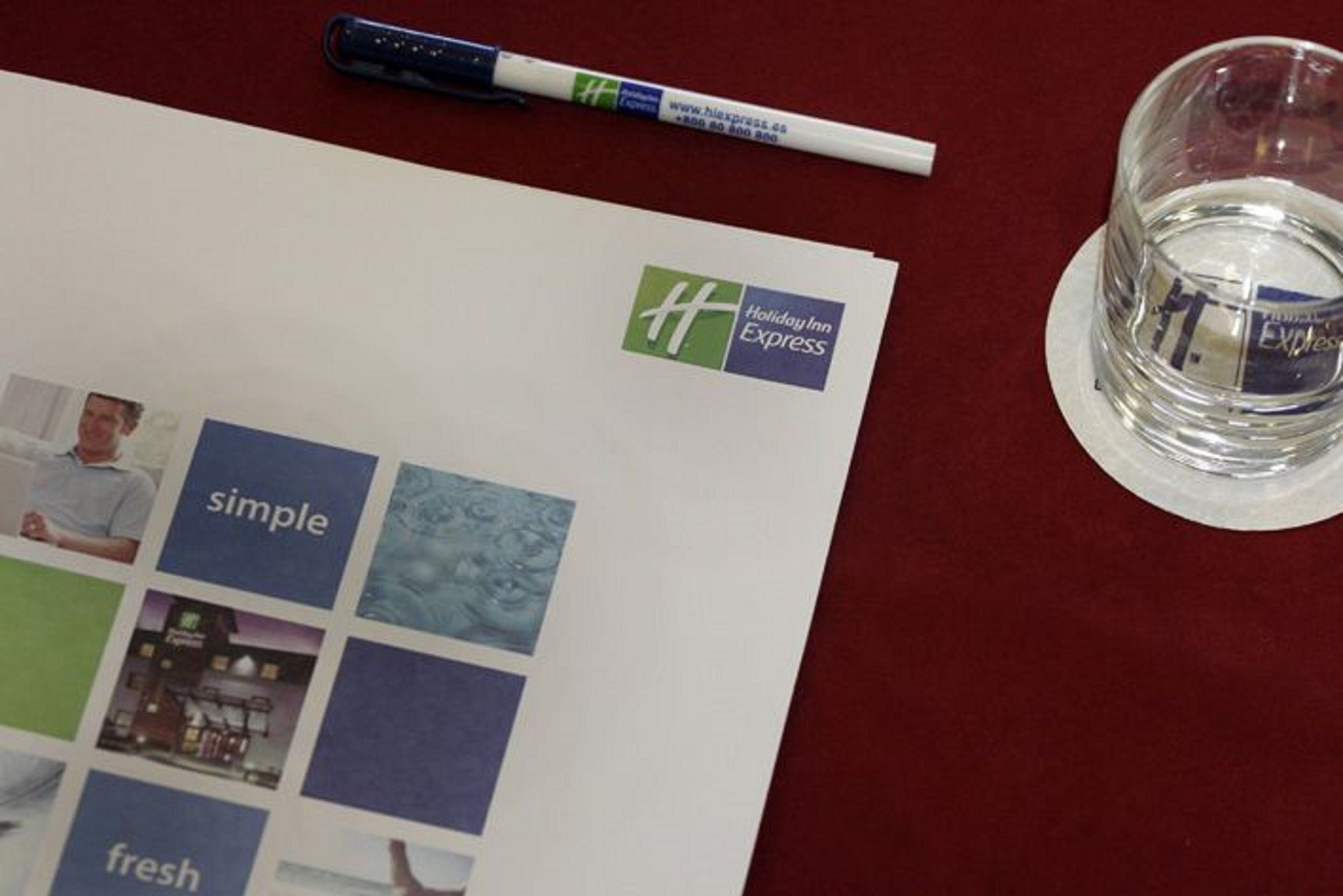 A brochure with the Holiday Inn Express logo, a pen, and a glass of water on a table.