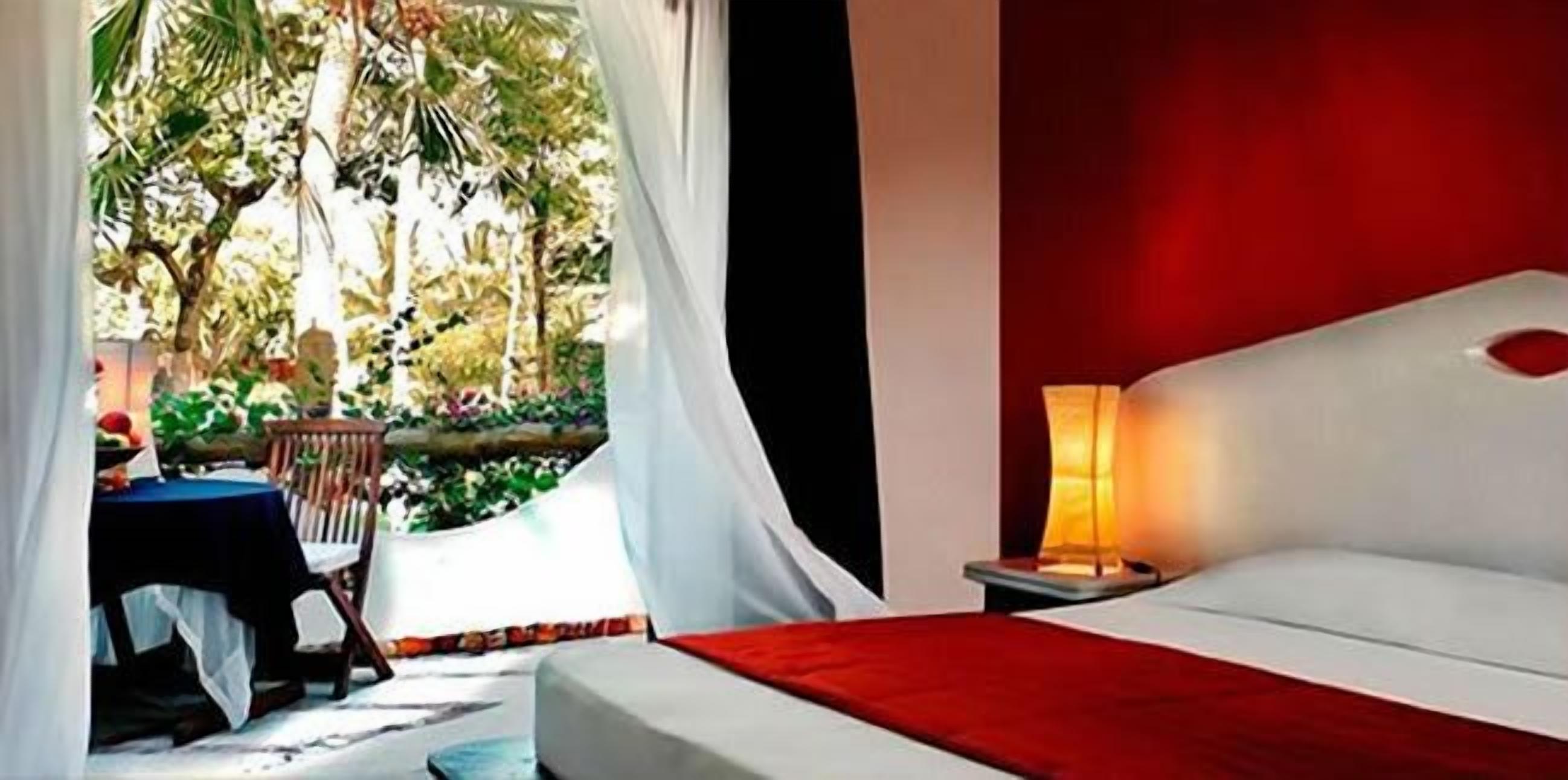 A bedroom with a bed, a nightstand, a table with chairs, and a view of a garden.